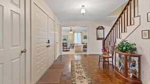 A hallway with wooden flooring, a rug, a staircase with a wooden railing, and a glass display cabinet with plants.