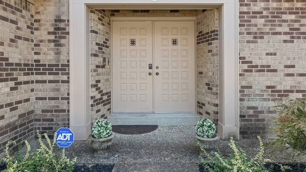A beige double door with a small window above it, set in a brick wall.