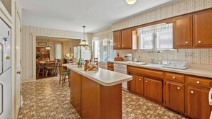 A kitchen with wooden cabinets, a central island, and a dining area with chairs and a table.