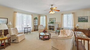 A spacious living room with a fireplace, a ceiling fan, and a large window.