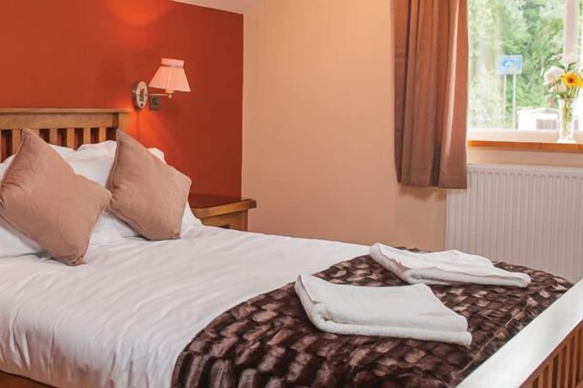 A neatly made bed with a wooden headboard, two bedside lamps, a bedside phone, and a window with curtains.