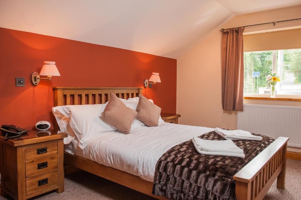 Une chambre à coucher avec un lit en bois, deux lampes de chevet, une table de chevet avec un téléphone et une horloge, et une fenêtre avec des rideaux.