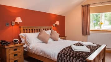 Un dormitorio con cama de madera, dos lámparas de noche, una mesita de noche con un teléfono y un reloj, y una ventana con cortinas.