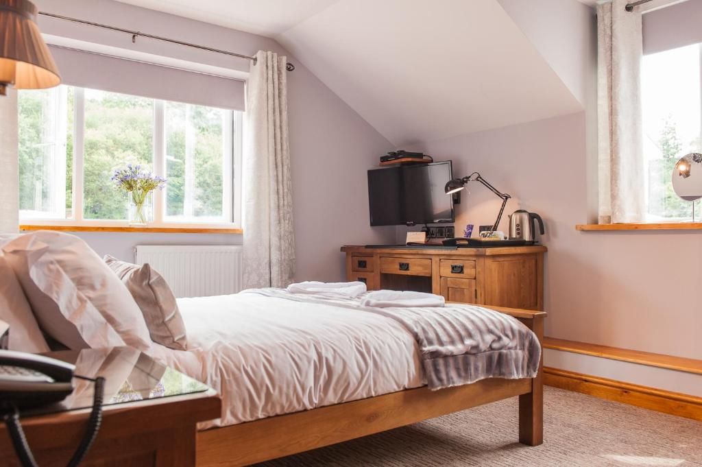 A bedroom with a bed, a desk with a computer, a television, and a window with curtains.