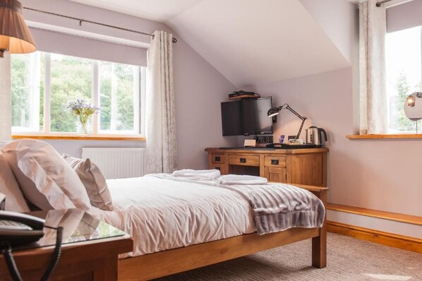Un dormitorio con una cama, un escritorio con computadora, televisor y ventana con cortinas.