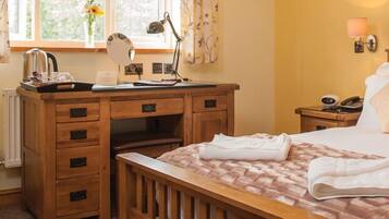 A neatly arranged bedroom with a wooden bed, a bedside table with a lamp, a nightstand with a phone, and a window with curtains.