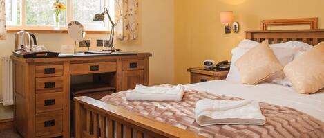 A neatly arranged bedroom with a wooden bed, a bedside table with a lamp, a nightstand with a phone, and a window with curtains.