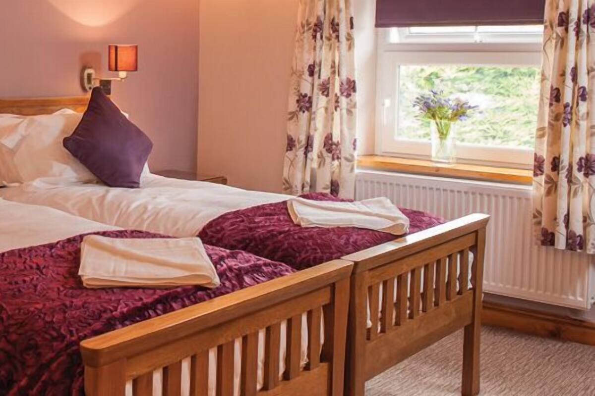 A double bed with two pillows, a bedside table with a lamp, and a window with curtains.