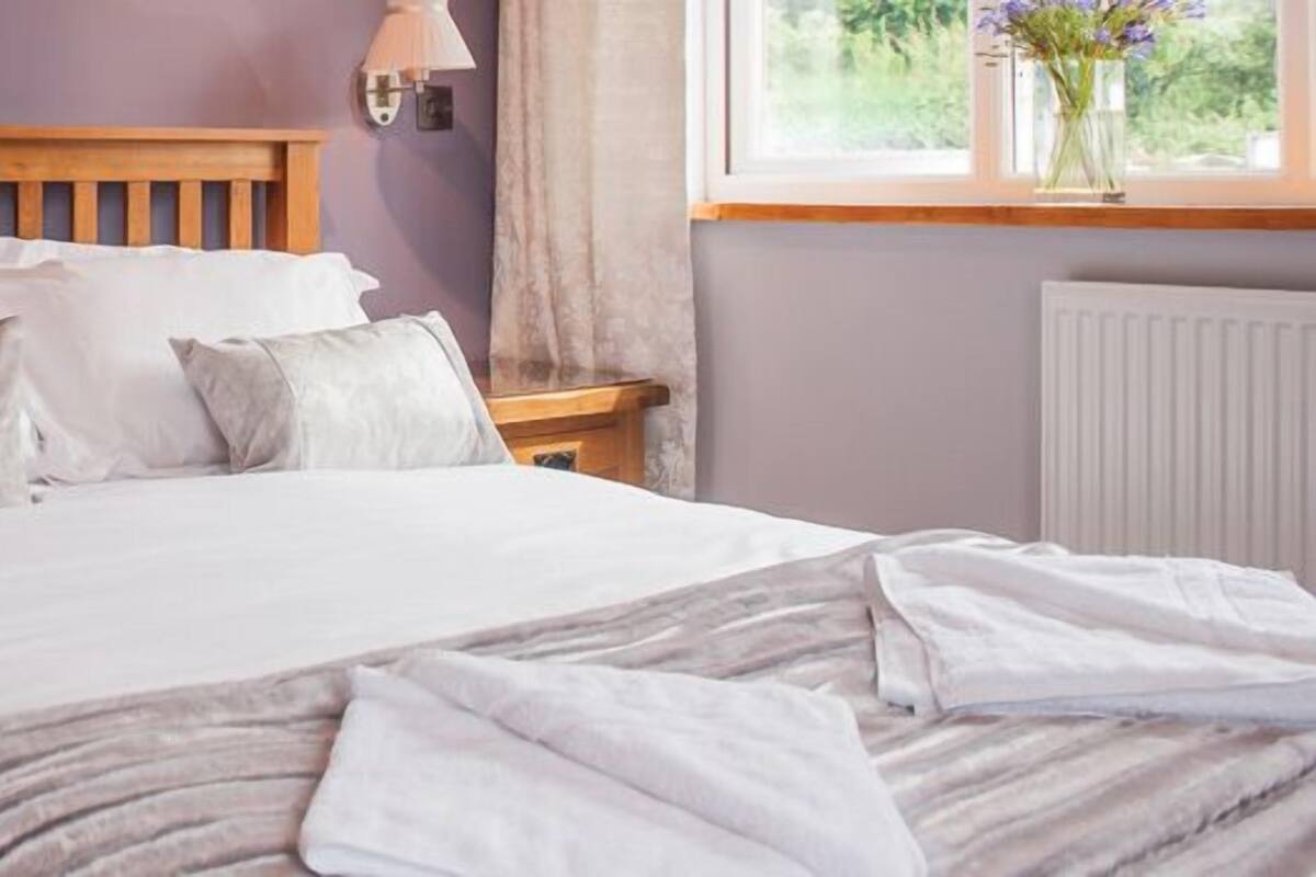 A neatly made bed with white linens and a wooden headboard in a room with purple walls.