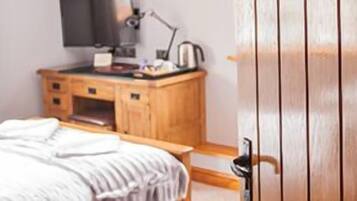 A bedroom with a wooden desk, a bed with a white comforter, and a wooden door.