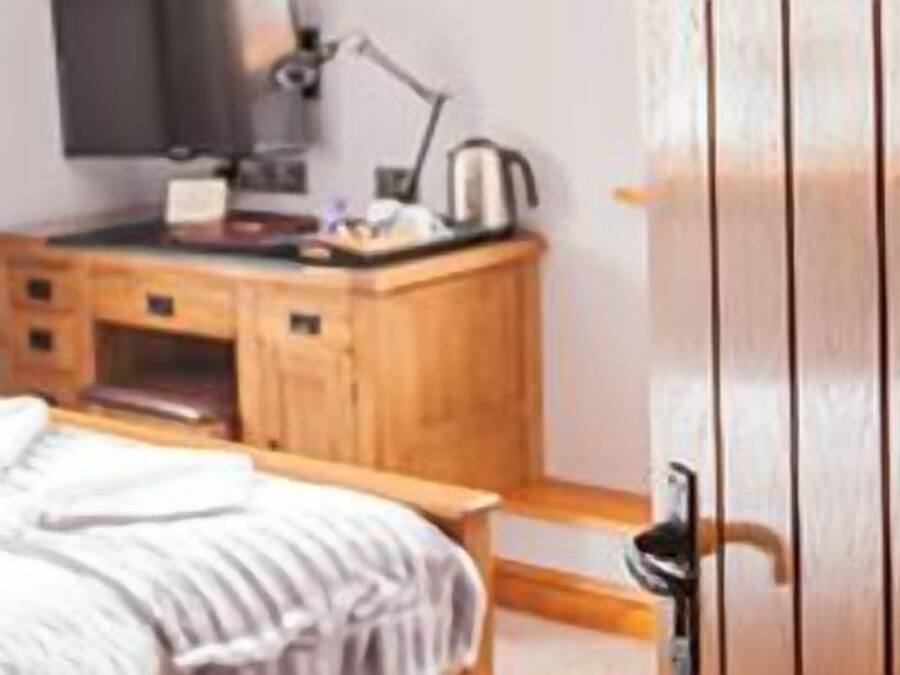 A bedroom with a wooden desk, a bed with a white comforter, and a wooden door.