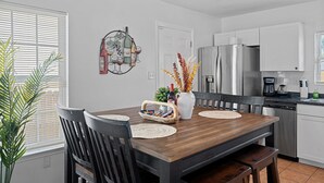 A modern kitchen with white cabinets, a stainless steel refrigerator, and a dining area with a wooden table and chairs.
