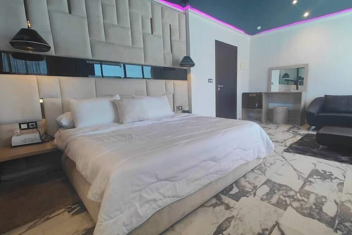 A modern bedroom with a large bed, bedside tables, a sofa, and a mirror.