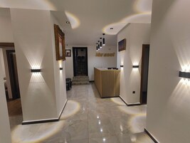Um hall de hotel moderno com uma mesa de recepção, luminárias fixadas na parede e piso ladrilhado.