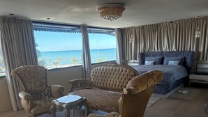 Un dormitorio lujoso con una cama grande, dos sillones decorativos, una mesita y vista al mar.