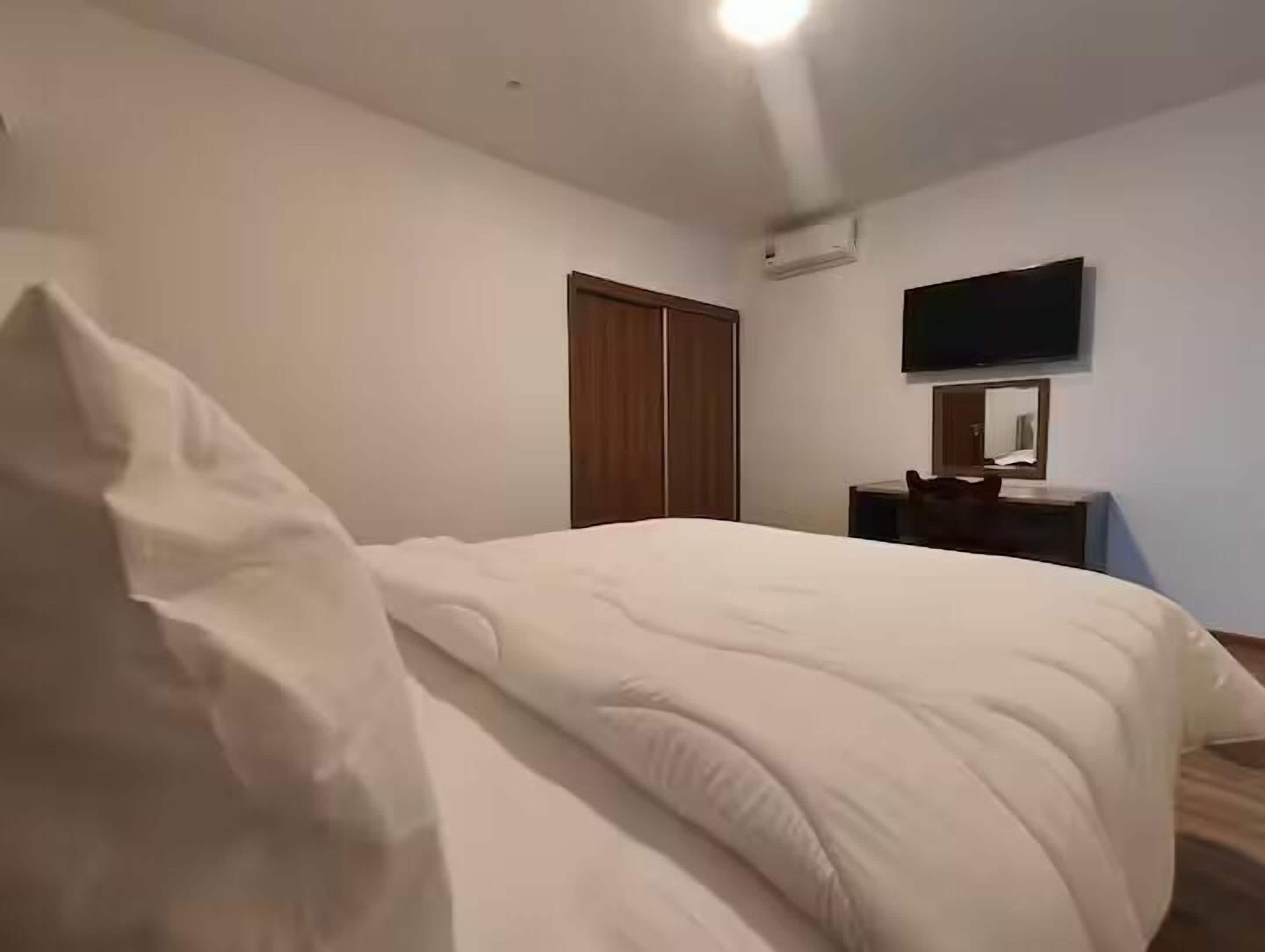 A bedroom with a bed, a wooden wardrobe, a flat-screen TV, and a small table.