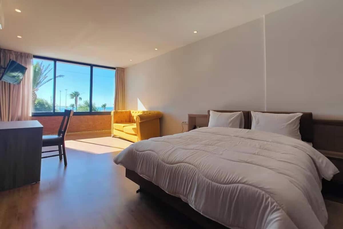 A modern hotel room with a large bed, a desk, and a sofa.