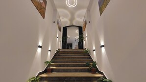 Un pasillo bien iluminado con escaleras de mármol, plantas en macetas y obras de arte en las paredes.