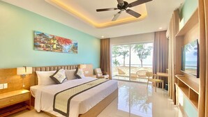 A hotel room with a bed, a ceiling fan, a painting, and a view of the beach.