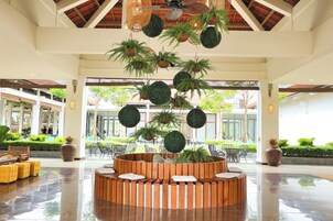 A spacious lobby with a central wooden planter, hanging plants, and a ceiling fan.