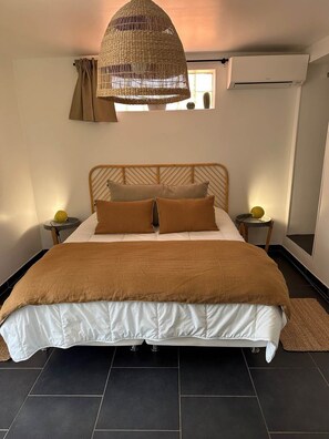 Ein Schlafzimmer mit einem großen Bett, einer gewebten Deckenleuchte, einem Nachttisch mit Lampe und einem Fenster mit Vorhängen.