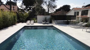A rectangular swimming pool with clear water, surrounded by a tiled deck and lounge chairs.
