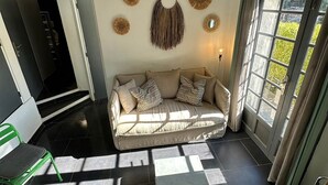 Un salon moderne avec un canapé, une petite table et un fauteuil vert. On y trouve des éléments décoratifs accrochés au mur et une fenêtre avec des rideaux.