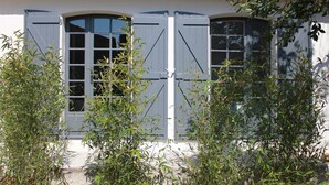 Un bâtiment à la façade blanche et aux volets sombres, entouré de verdure.