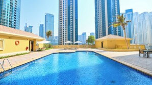Una piscina con un edificio amarillo y palmeras en primer plano, rodeada de altos edificios modernos.