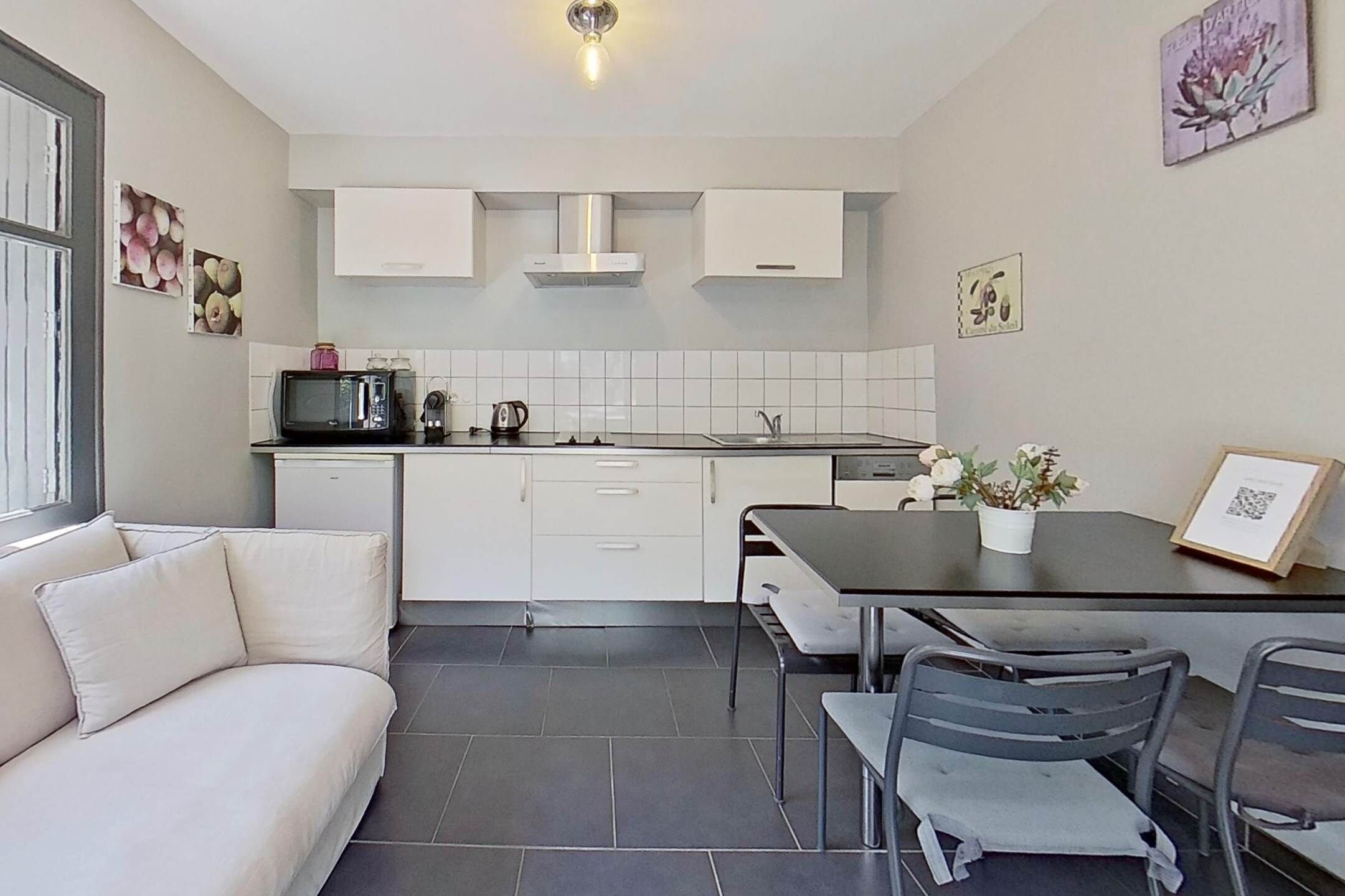 A modern kitchen with white cabinets, a black countertop, and a dining area with a table and chairs.