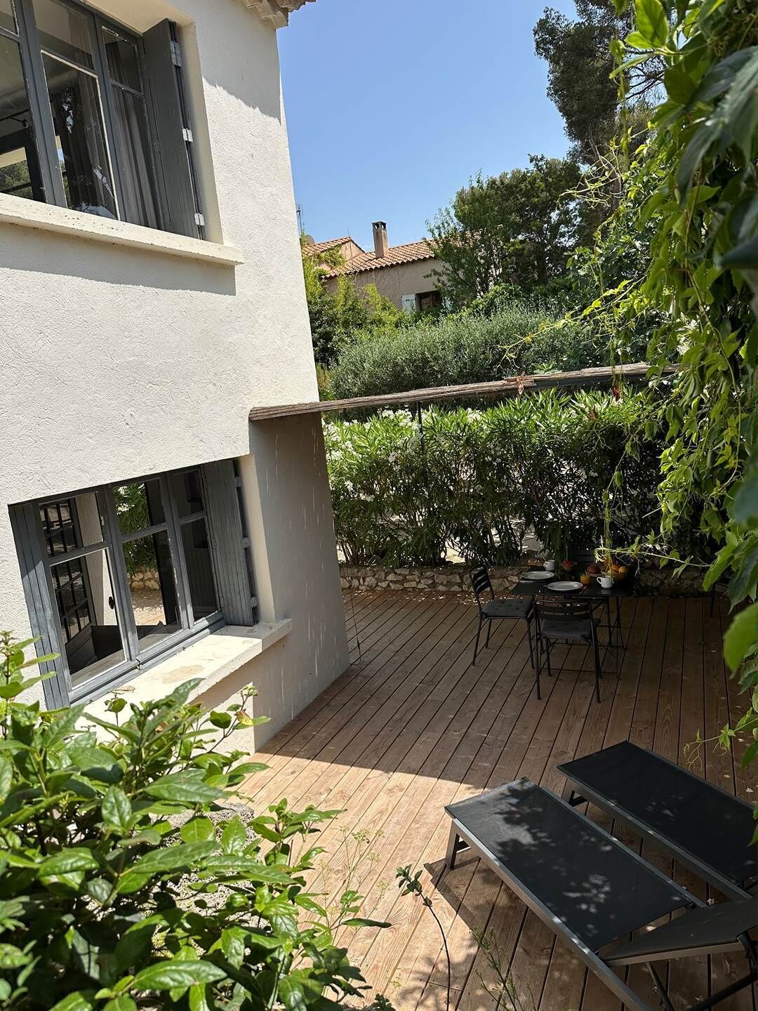 Un espace patio avec une terrasse en bois, une table et des chaises, et un petit jardin avec différentes plantes.