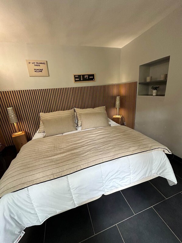 A hotel room with a bed, a sign reading "Bienvenue Welcome", and a small shelf with decorative items.