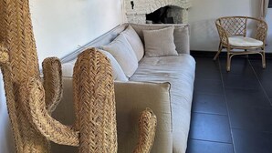 Un saló modern amb un sofà, dues cadires de vimbles, una obra decorativa a la paret i una finestra amb vista a edificis.