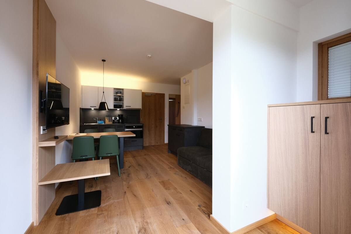 Una cocina moderna con armarios de madera, una mesa de comedor con sillas y un sofá negro en la sala de estar.