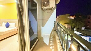 A balcony with a sliding glass door, an air conditioning unit, and a view of the cityscape at night. - RB INTERNATIONAL - PURI near Sea Beach (Puri)