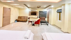 A hotel room with two beds, a sofa, a dining table, and a TV. - RB INTERNATIONAL - PURI near Sea Beach (Puri)