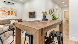 Un salon moderne avec une table à manger en bois, des tabourets de bar noirs, un canapé gris et une table basse.