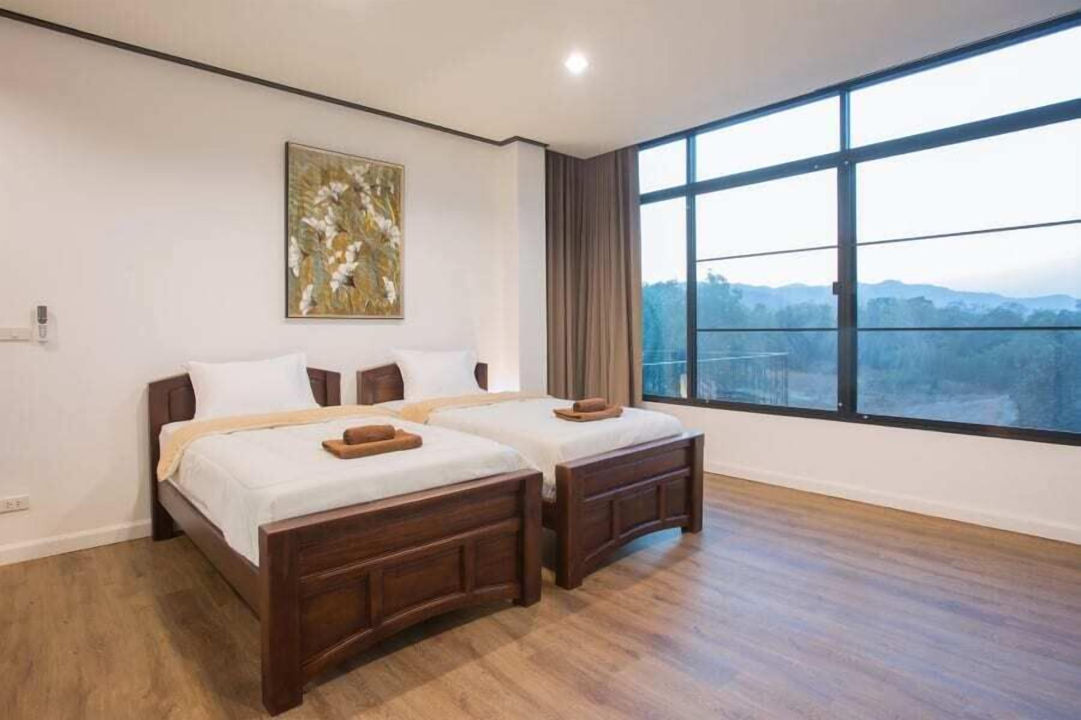 Un dormitorio con dos camas de madera, un ventanal con vistas a las montañas y un cuadro en la pared.