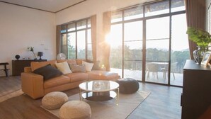 Una sala moderna con sofá, mesa de centro y reposapiés, ventanas amplias con vistas y un balcón.