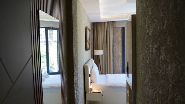 A hotel room with a bed, bedside table, lamp, and a view of the outdoors through a window. - Sword Suit Hotel (Istanbul)