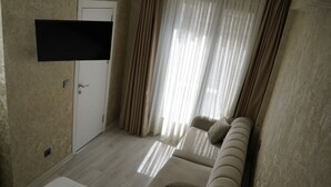 A room with a beige sofa, a flat-screen TV mounted on the wall, a door, and sheer curtains. - Sword Suit Hotel (Istanbul)