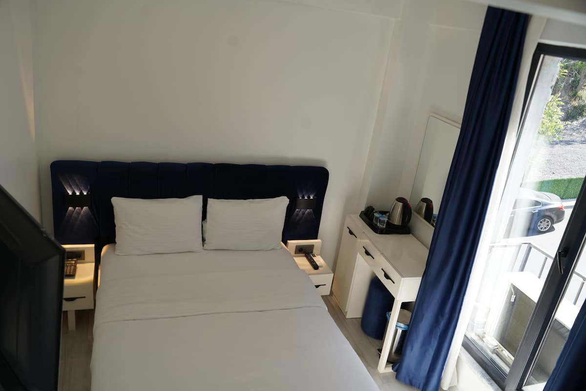 Habitación de hotel con cama, mesitas de noche, escritorio y ventana con cortinas.