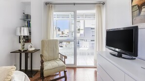 A room with a large window, a television, a chair, and a small table with a lamp. - A&N California (Torre del Mar)