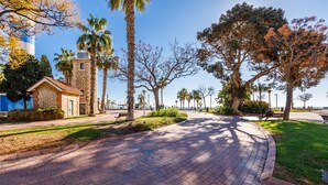 A paved pathway with benches, palm trees, and a small stone building. - A&N California (Torre del Mar)