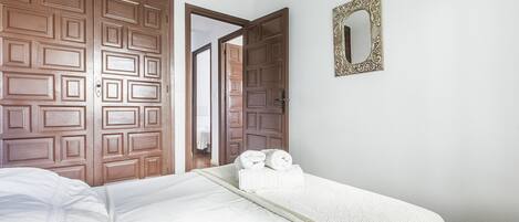 Habitación de hotel con un amplio armario de madera, una cama con ropa blanca y un espejo decorativo en la pared.
