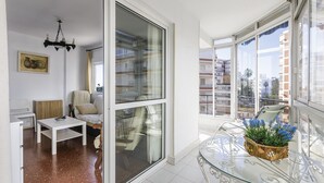 A modern apartment with a glass sliding door, a white sofa, a small table, and a balcony with a glass table and potted plants. - A&N California (Torre del Mar)