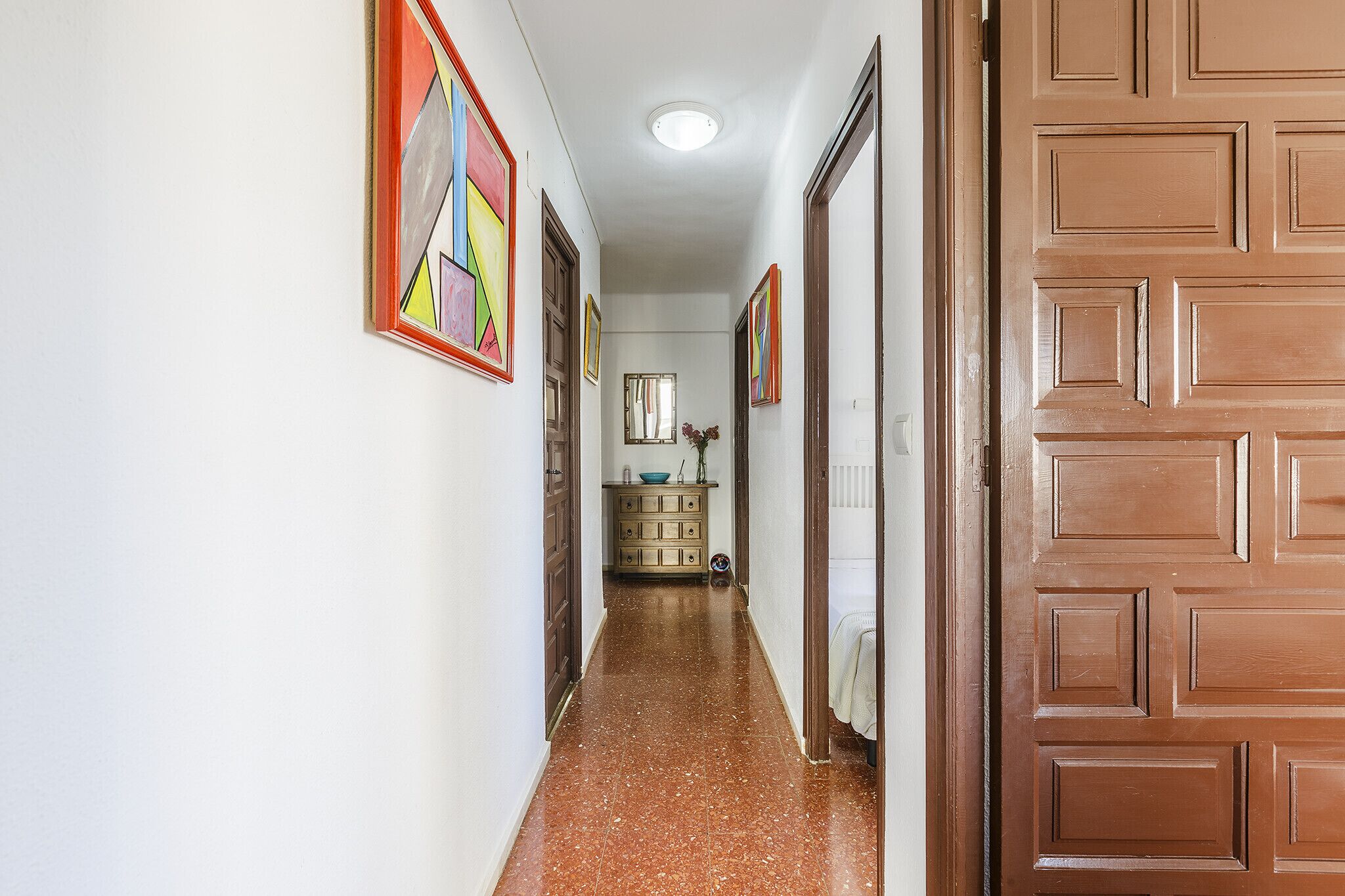 A hallway with a tiled floor, wooden doors, and colorful artwork on the walls.