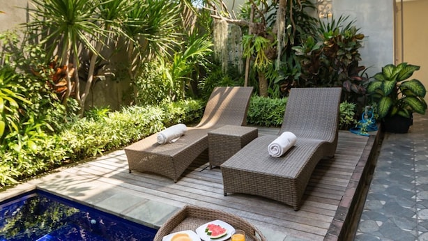 An outdoor pool area with lounge chairs and a dining table set with food and drinks. - Kubu Ramah Canggu (Tibubeneng)