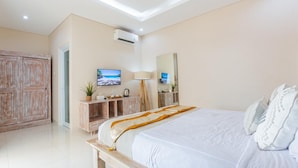 A bedroom with a large bed, wooden furniture, a television, and a mirror. - Kubu Ramah Canggu (Tibubeneng)