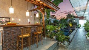A bar area with a brick wall, wooden chairs, hanging lights, and a poolside with potted plants. - Kubu Ramah Canggu (Tibubeneng)
